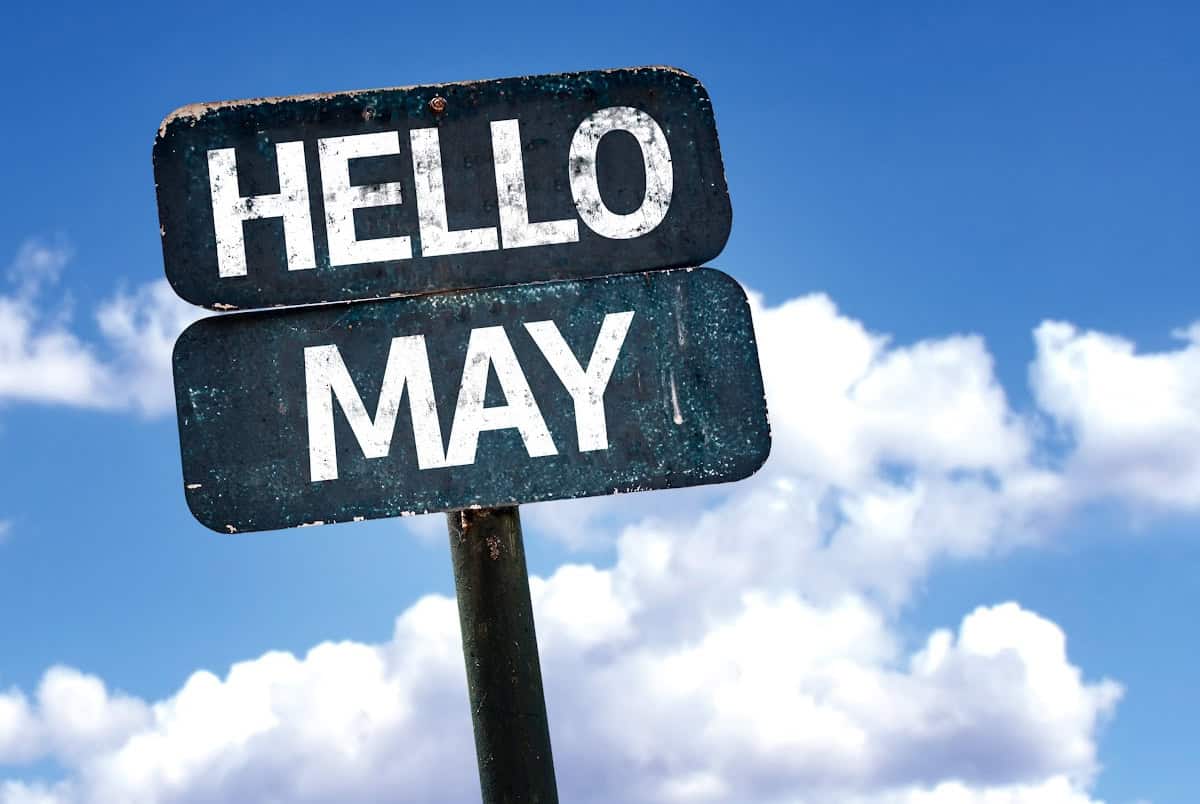 A street sign with HELLO MAY in bold white letters stands against a blue sky with scattered white clouds.