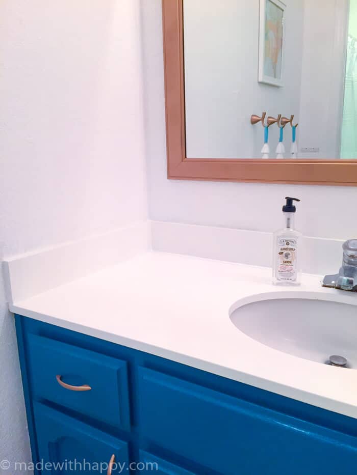 50 dollar bathroom makeover.  We turned this off-white and brown 80's bathroom into a modern dream with just a few changes.  We were able to paint the tile and paint the vanity top changing the look of the bathroom dramatically.  Bathroom Makeover on a budget.  DIY Bathroom.  Modern Blue Bathroom.  www.madewithhappy.com