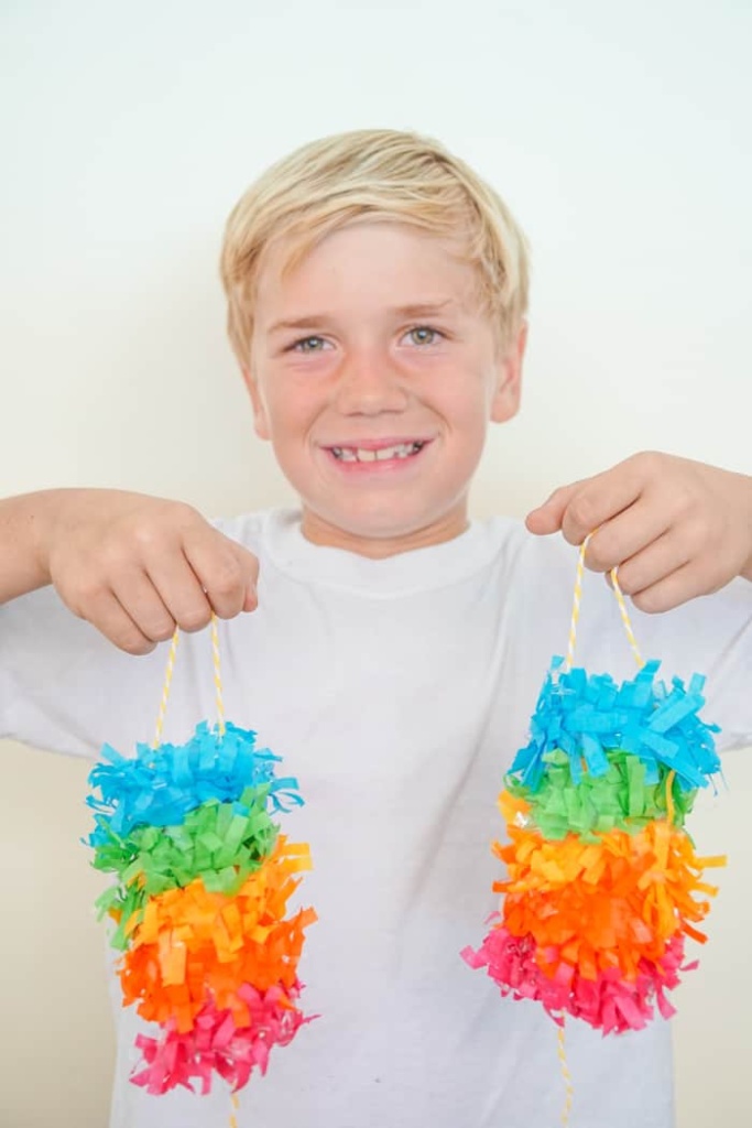 boy holding two mini rainbow pinatas