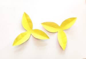 Two yellow, paper cut-outs resembling flower petals are placed on a white background. The shapes have three and four pointed edges, respectively, with slight creases suggesting a crafted texture.