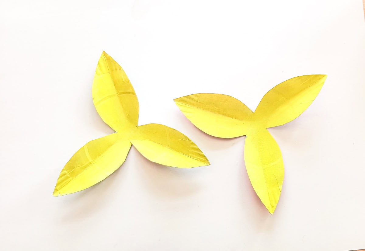 Two yellow, paper cut-outs resembling flower petals are placed on a white background. The shapes have three and four pointed edges, respectively, with slight creases suggesting a crafted texture.