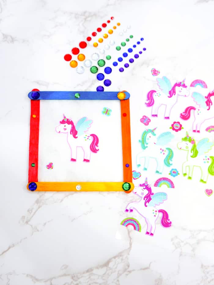 Once the Elmer’s glue has dried on each frame, begin decorating your parchment paper with the unicorn stickers, and decorate your frame with the adhesive gemstones.