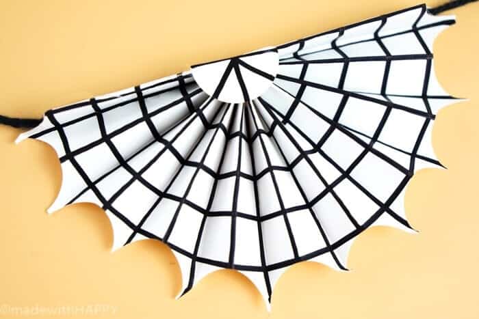 Spookify your space with this super cute spider web garland.  These are simple Halloween Decorations made out paper and a pen.  Non-scary Halloween decorations are great for houses with young kids or classrooms.  www.madewithhappy.com