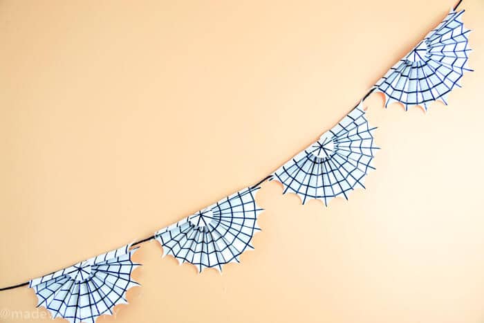 Spookify your space with this super cute spider web garland.  These are simple Halloween Decorations made out paper and a pen.  Non-scary Halloween decorations are great for houses with young kids or classrooms.  www.madewithhappy.com