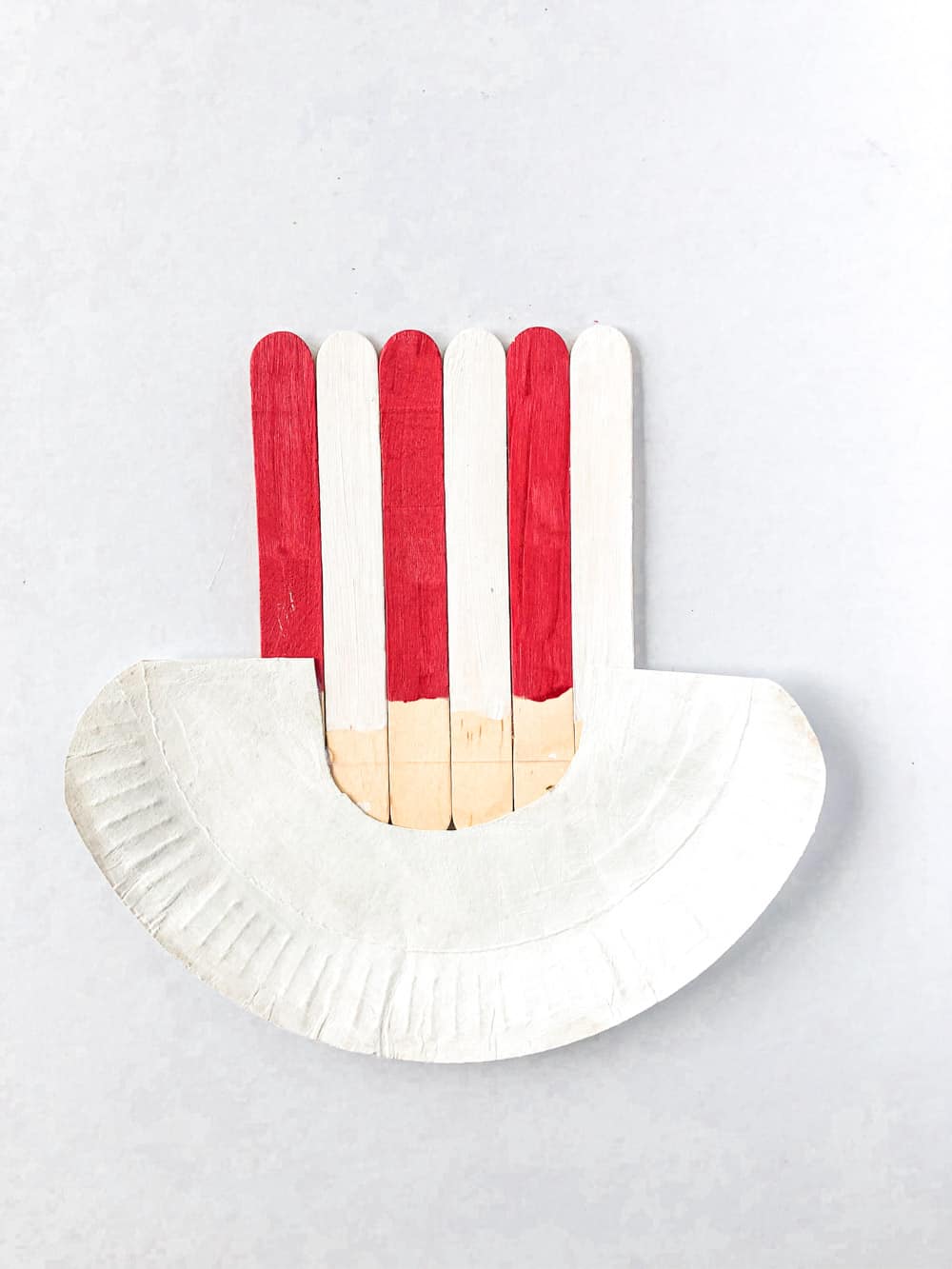 Align them together, the popsicle sticks above, the blue popsicles in the middle and the paper plate below them, and glue them using the glue gun.