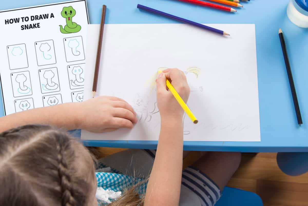 A child draws a snake on white paper using colored pencils at a blue table. A drawing guide titled How to Draw a Snake is beside them, showing step-by-step illustrations.