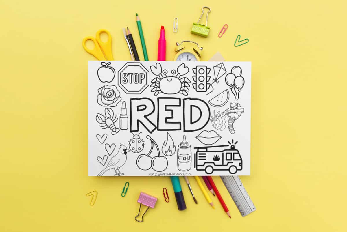 A coloring sheet with the word RED surrounded by images of a crab, stop sign, apple, and other red-themed items. Scattered around are markers, scissors, a ruler, a paper clip, and a binder clip on a yellow background.