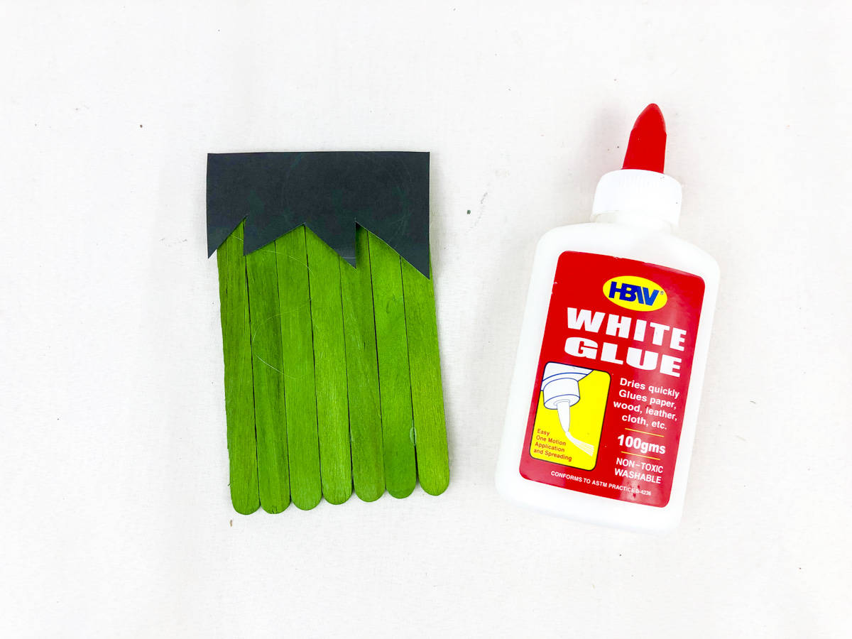 glue black paper hair to top of green craft sticks
