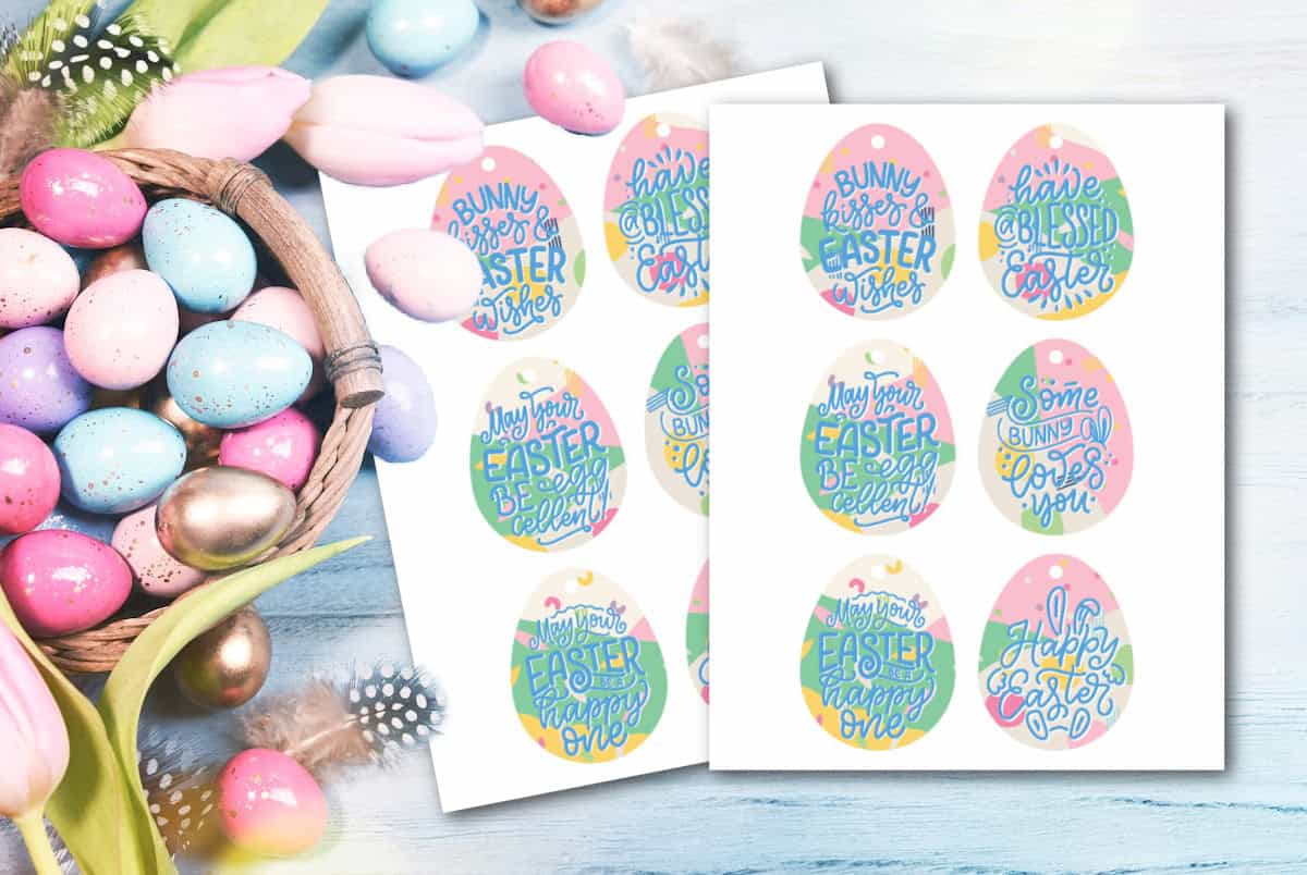 A wooden table with a basket of colorful Easter eggs and tulips. Next to it, sheets of paper display egg-shaped tags with pastel colors and festive phrases like Bunny kisses and Happy Easter.